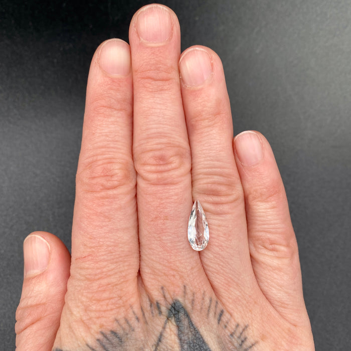 1.80 carat pear cut faceted Brazilian phenakite gemstone on hand to show size. available on sanctuaryofstones.com