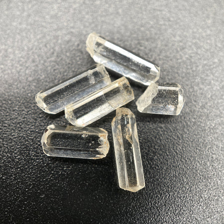 Top view of 6 pieces of Burmese phenakite hexagonal barrel stones on black background. available at sanctuaryofstones.com