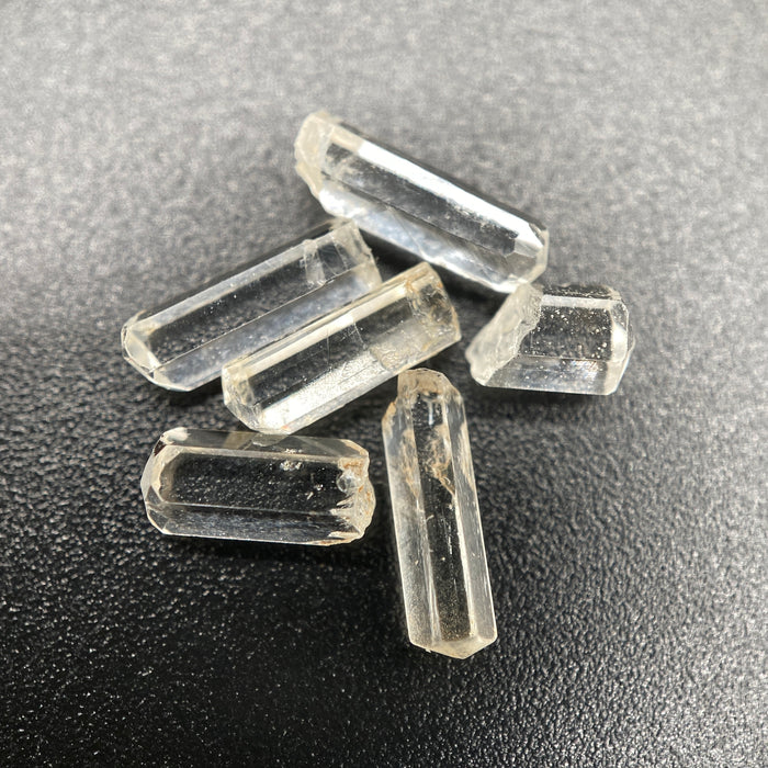 Top view of 6 pieces of Burmese phenakite hexagonal barrel stones on black background. available at sanctuaryofstones.com