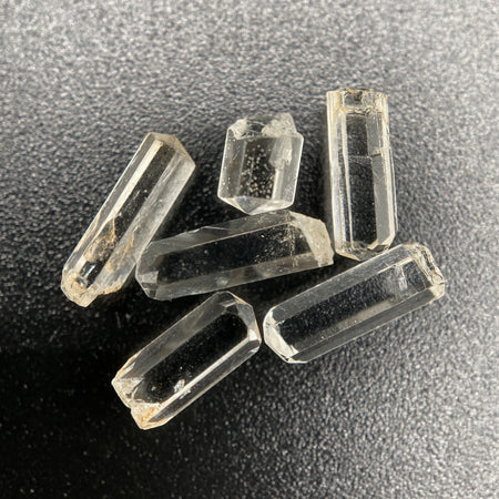 Top view of 6 pieces of Burmese phenakite hexagonal barrel stones on black background. available at sanctuaryofstones.com