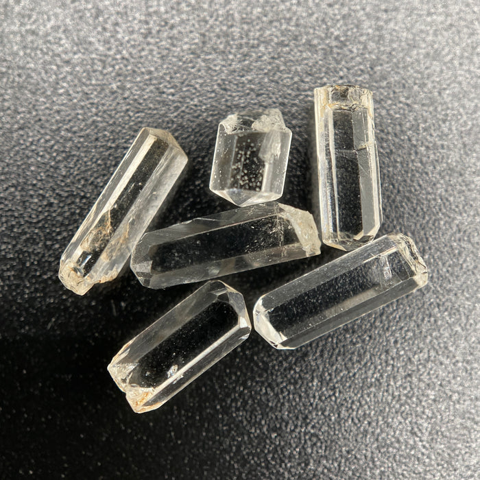 Top view of 6 pieces of Burmese phenakite hexagonal barrel stones on black background. available at sanctuaryofstones.com