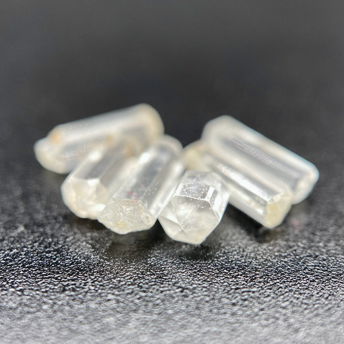 Top view of 6 pieces of Burmese phenakite hexagonal barrel stones on black background. available at sanctuaryofstones.com