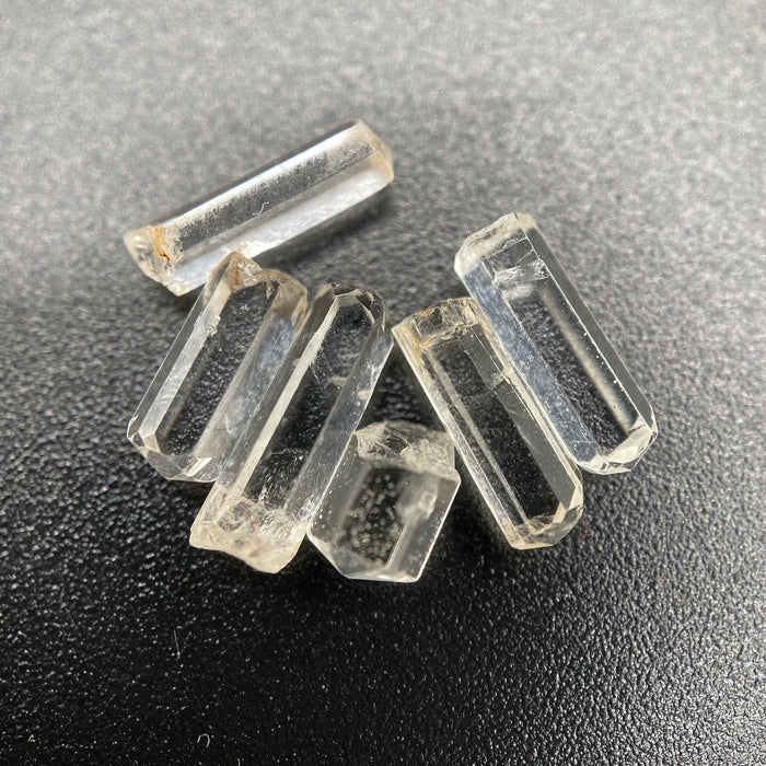 Top view of 6 pieces of Burmese phenakite hexagonal barrel stones on black background. available at sanctuaryofstones.com