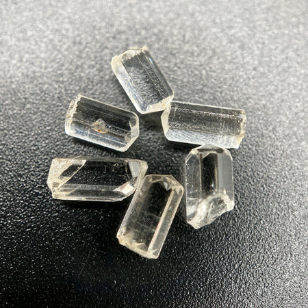 6-piece lot of Burmese phenakite hexagonal barrel crystals that are optically clear on black background available at sanctuary of stones dot com | sanctuaryofstones.com