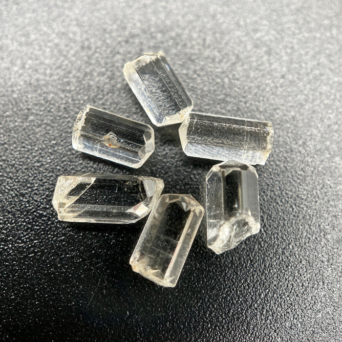 6-piece lot of Burmese phenakite hexagonal barrel crystals that are optically clear on black background available at sanctuary of stones dot com | sanctuaryofstones.com