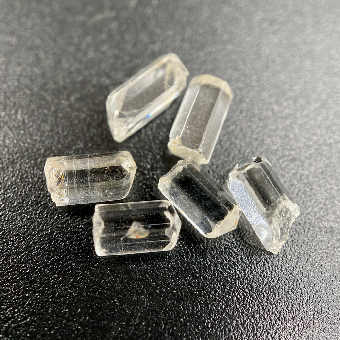 6-piece lot of Burmese phenakite hexagonal barrel crystals that are optically clear on black background available at sanctuary of stones dot com | sanctuaryofstones.com
