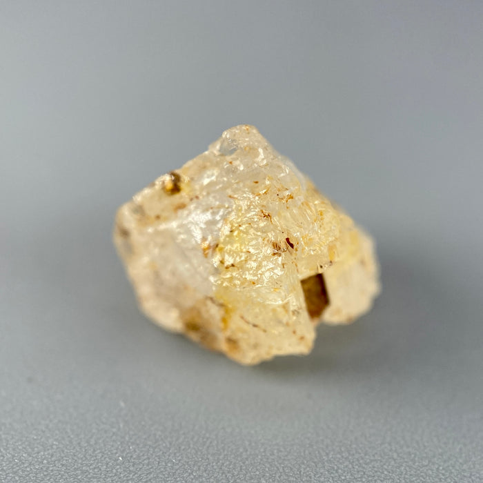 Etched rough Nigerian phenakite crystal with orange tint on grey background. available at sanctuaryofstones.com