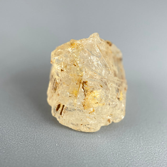 Etched rough Nigerian phenakite crystal with orange tint on grey background. available at sanctuaryofstones.com