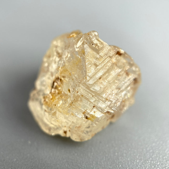 Etched rough Nigerian phenakite crystal with orange tint on grey background. available at sanctuaryofstones.com