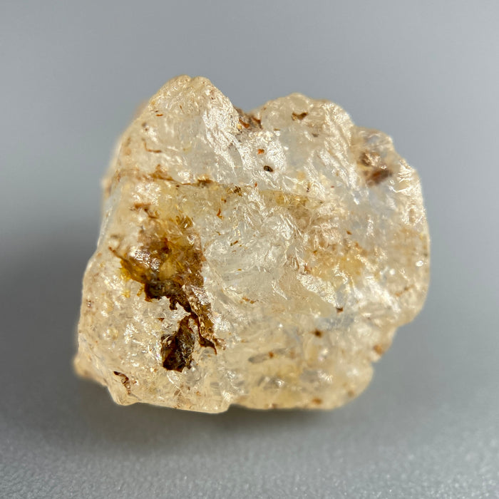Etched rough Nigerian phenakite crystal with orange tint on grey background. available at sanctuaryofstones.com