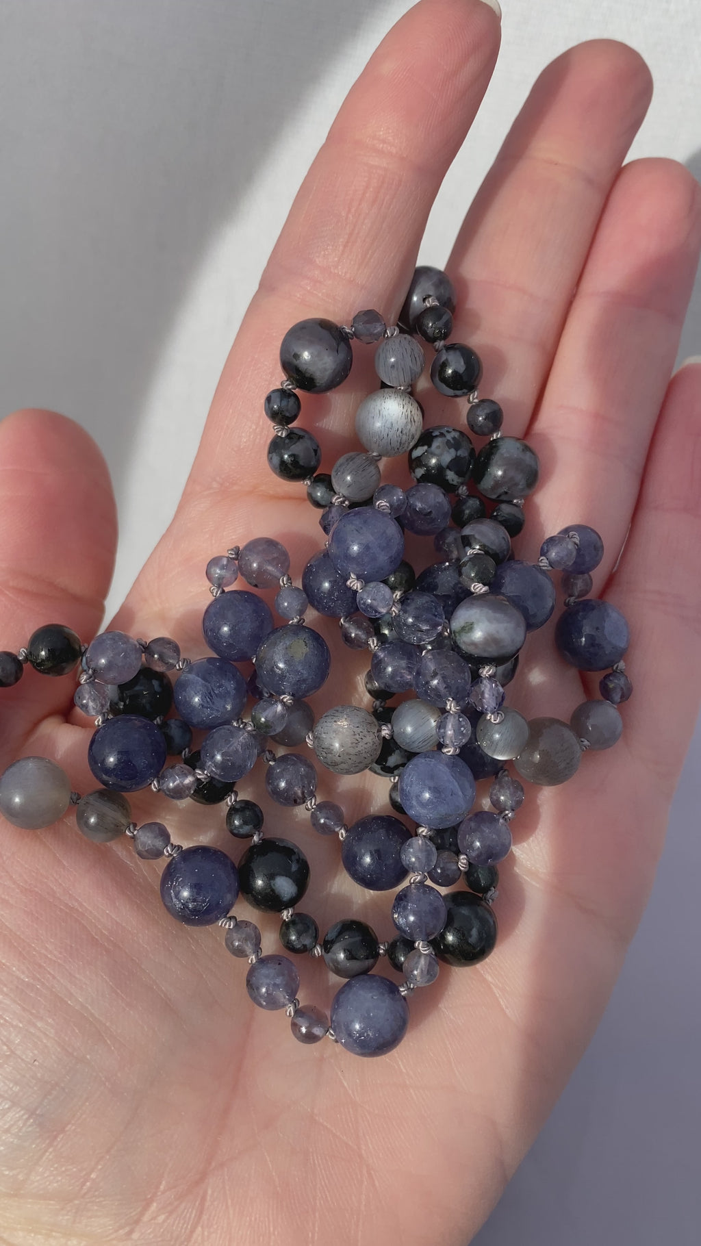 video of sanctuary vibrational jewelry's Harmonics of Light and Shadow hand-knotted beaded necklace with natural iolite rutilated gray moonstone and indigo gabbro